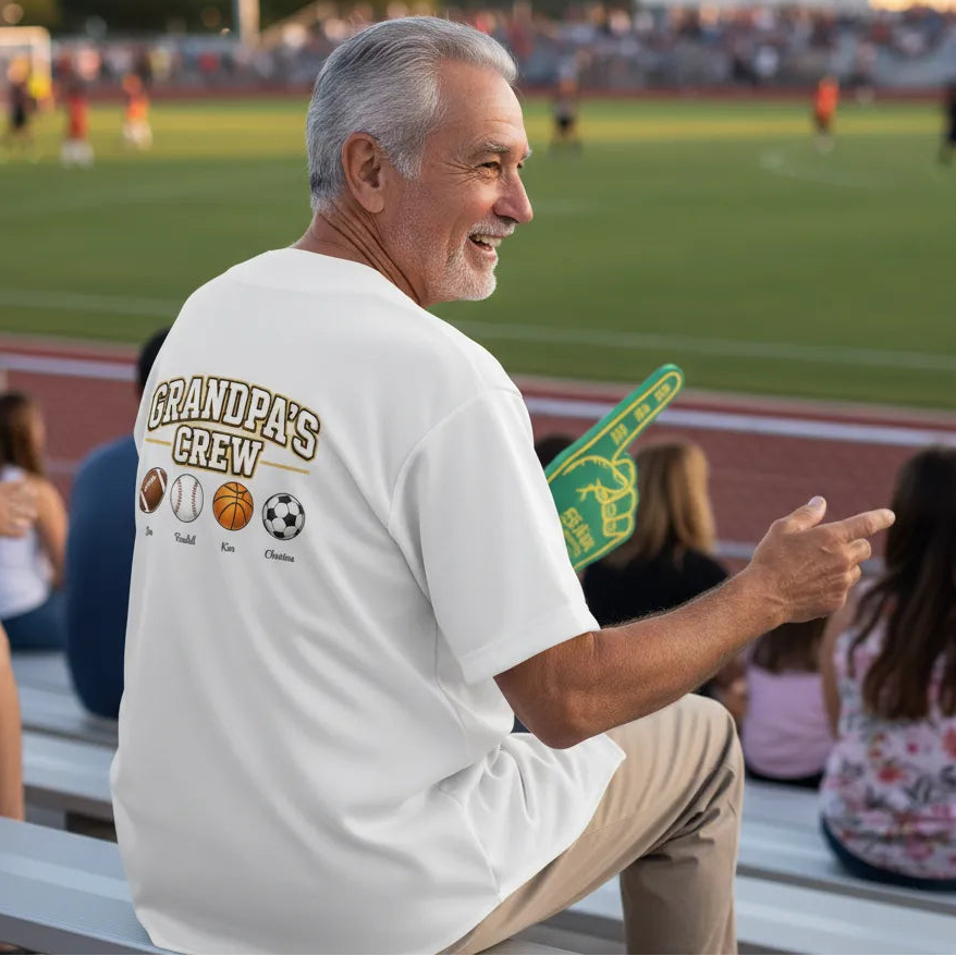 Man sitting on bleachers at a sports event, wearing a 'Grandpa's Crew' Custom Embroidered Baseball shirt. Love Life Journey
