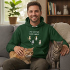 Man wearing a Custom My Siblings Have Paws Embroidered Adult Unisex Hoodie Pet Cats in Green, sitting on a couch with two cats.
