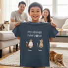 Child holding a t-shirt Personalized My Siblings Have Paws kids T-shirt featuring custom cat characters and cat names in a living room with family and cats.