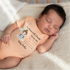 Newborn baby wearing a peach onesie Personalized Welcome To The Family baby bodysuit featuring custom baby character and birth date calendar, lying on a soft surface.